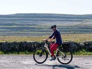 biking lady on an eBike with burren hills in the background.